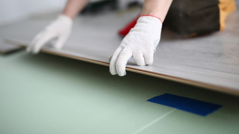 person with gloves installing floating floor boards on top of green underlaying material