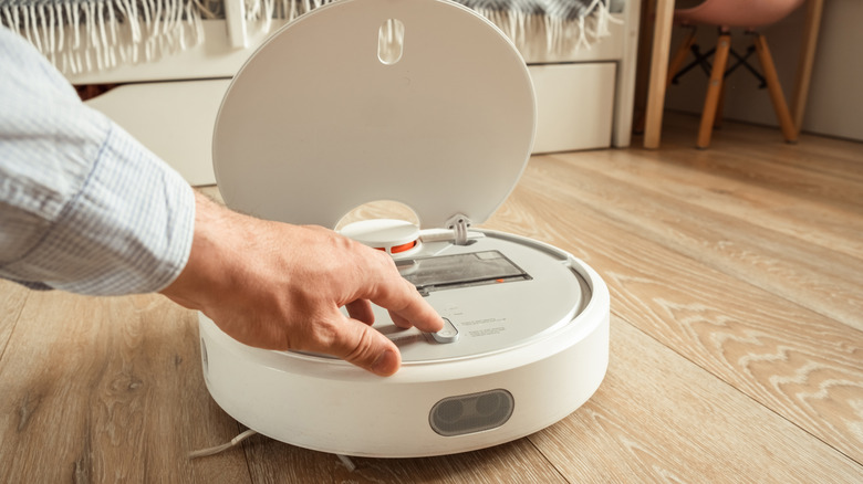 A person opening the top portion of a robot vacuum