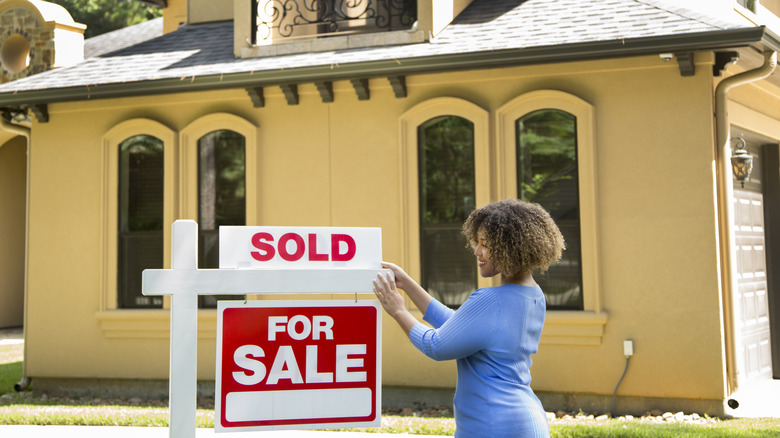 woman hanging house sold sign