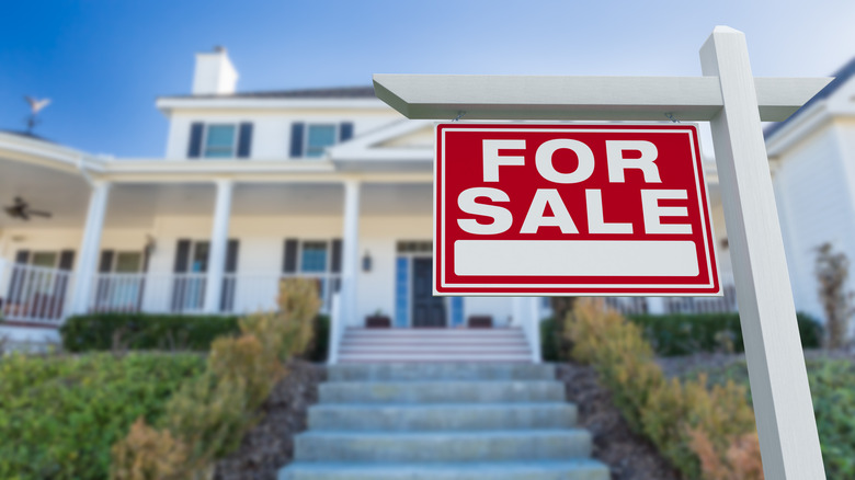 A "For Sale" sign is in front of a large white house