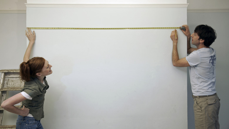 Woman and man measuring a white wall.