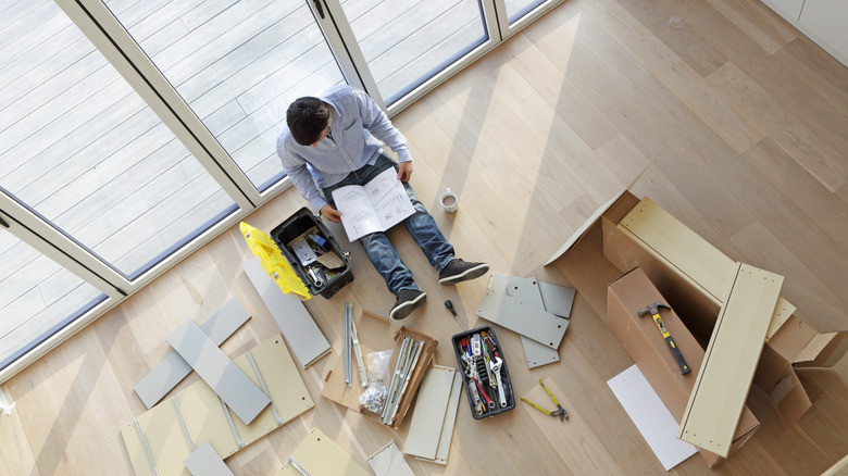 Man surrounded by tools and materials reads assembly instructions