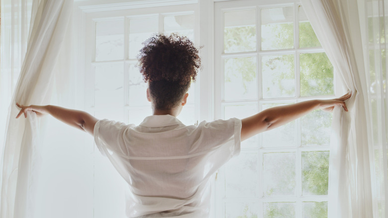 Woman opening white curtains