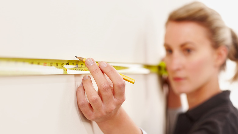 Woman marking the wall with a measuring tape