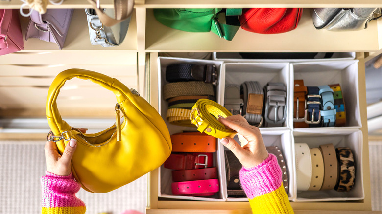 Top view of woman holding yellow purse against backdrop of belts and bags