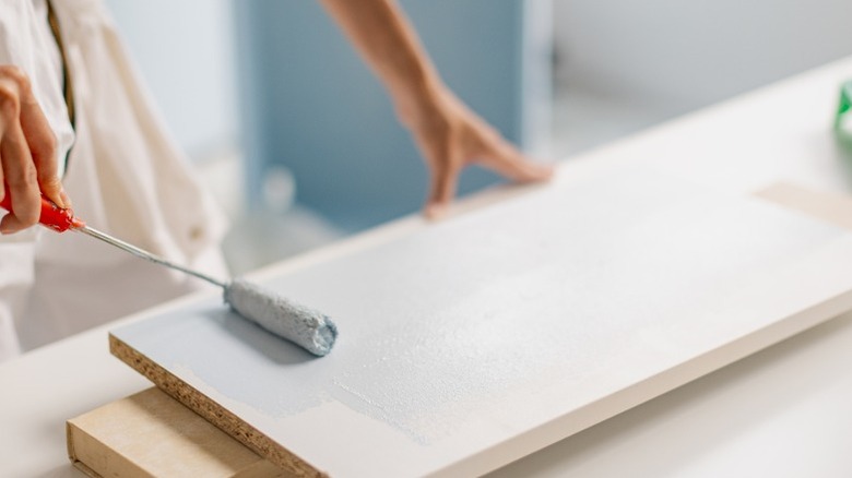 person painting white IKEA furniture panel with small roller