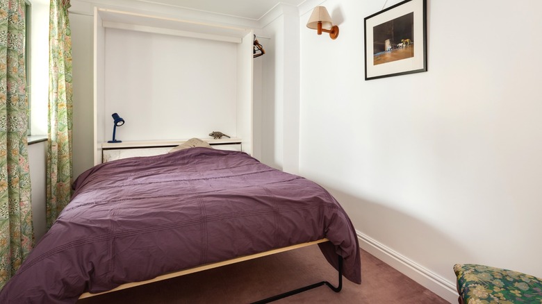 Purple comforter on murphy bed in small bedroom with green floral accents