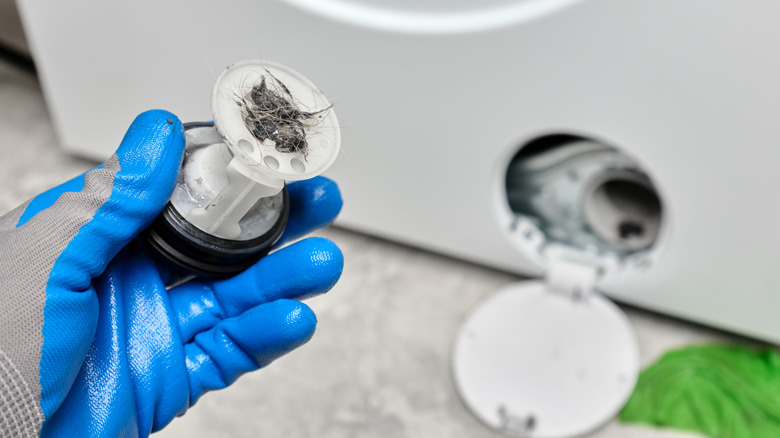 Gloved hand holding a washing machine filter full of pet hair and debris