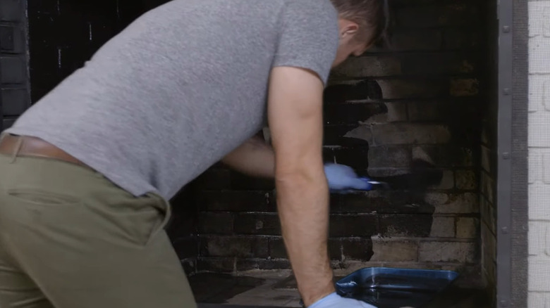 Man painting inside of fireplace with black paint on roller.