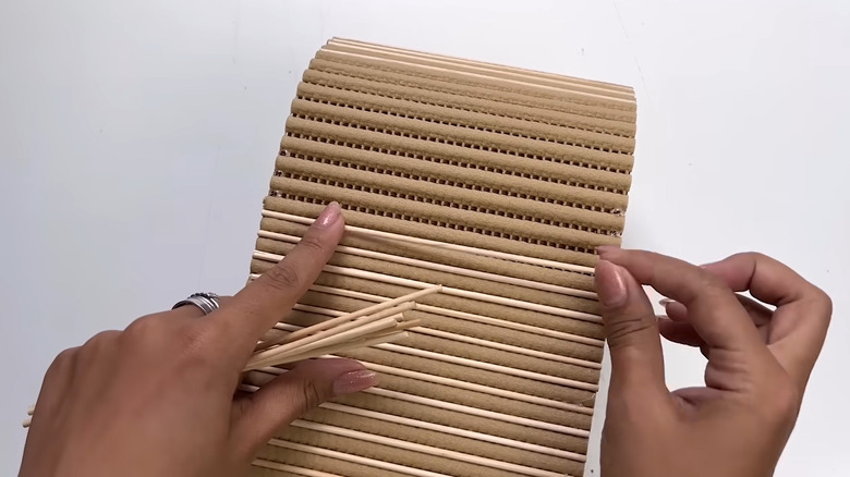 Crafter gluing pieces of bamboo skewer to the exterior of homemade basket