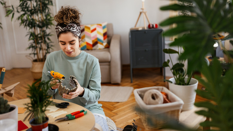 Brown-haired woman crafting with a glue gun in living room