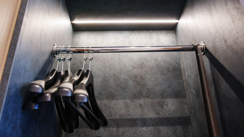 Empty coat hangers hang in an empty closet with black walls lit from above