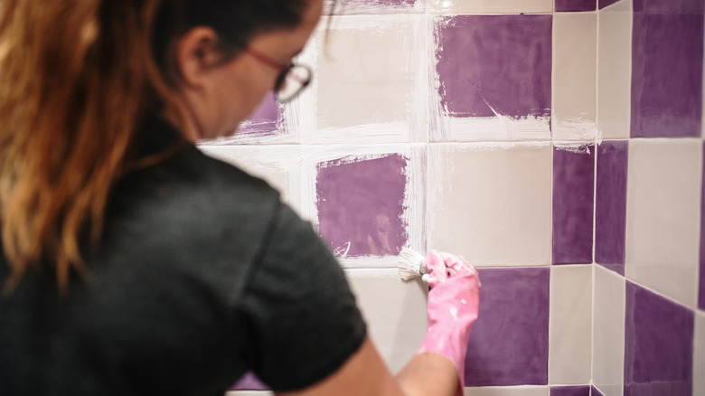 A woman painting shower tiles with a paint brush