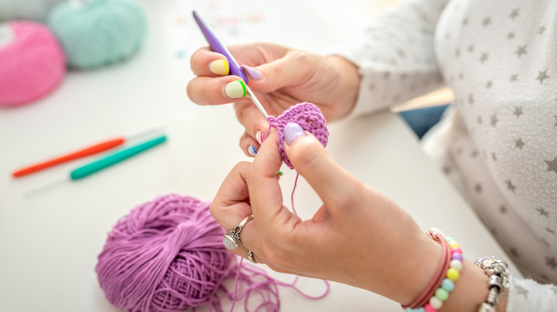 Female hands seen crocheting with purple yarn