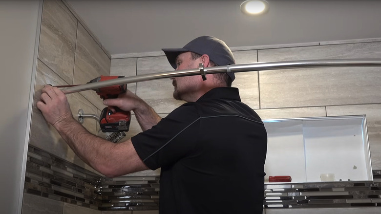 Handyman uses a drill to install a shower curtain on tile