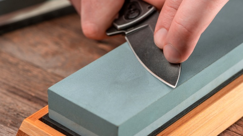 person sharpening pocketknife with whetstone