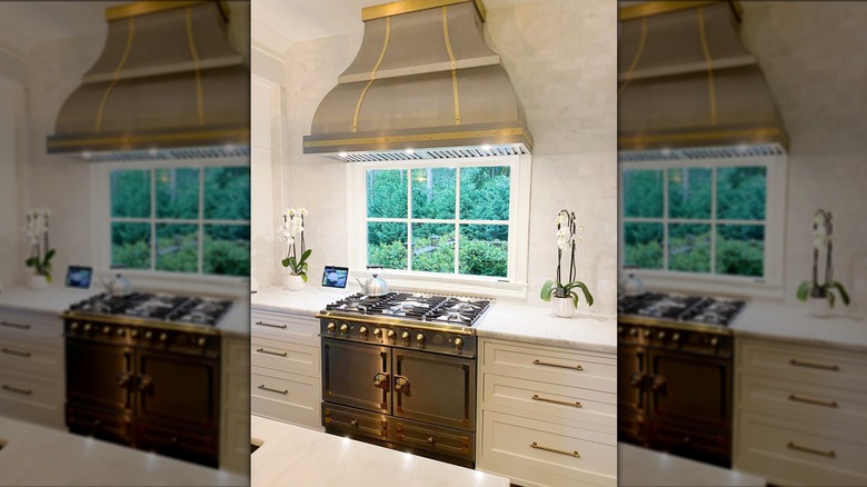 A kitchen has a curved range hood with brass accents