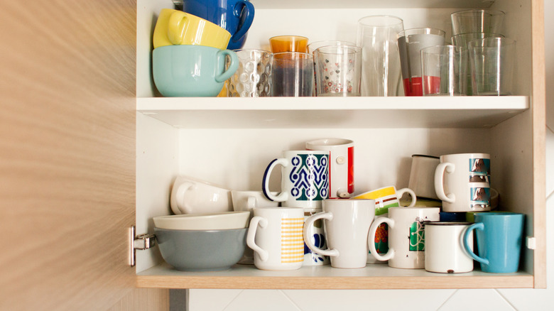 Kitchen cabinet overflowing with glasses and stacked coffee mugs