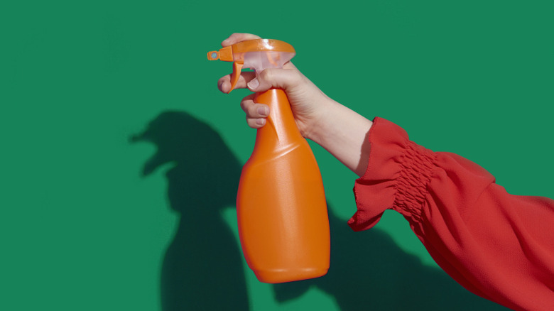 A hand holds a spray bottle up to a wall.