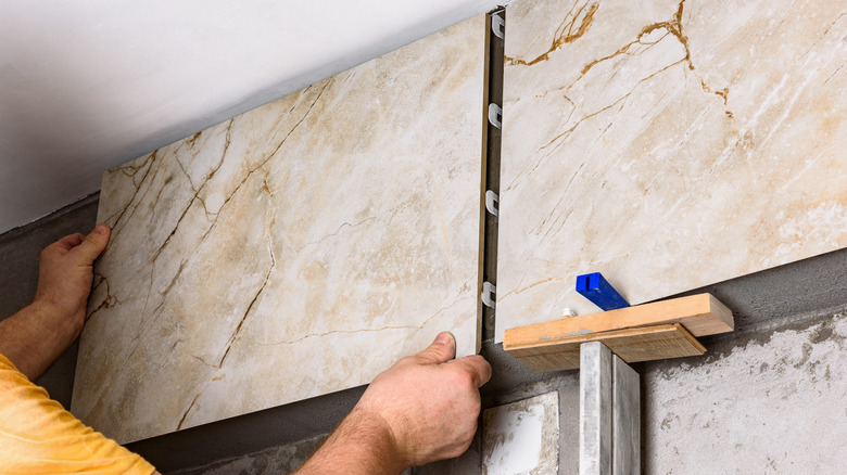 Person installing large format tiles on wall