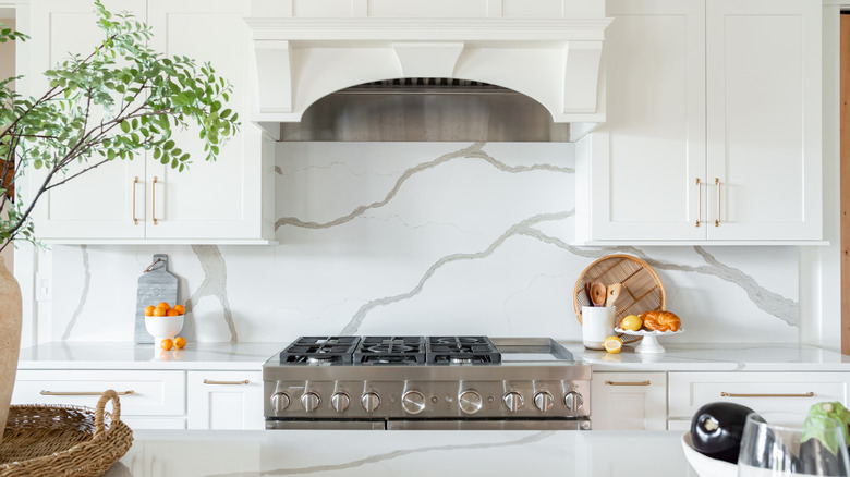 Chic white kitchen with marble slab counters and matching, full-height backsplash