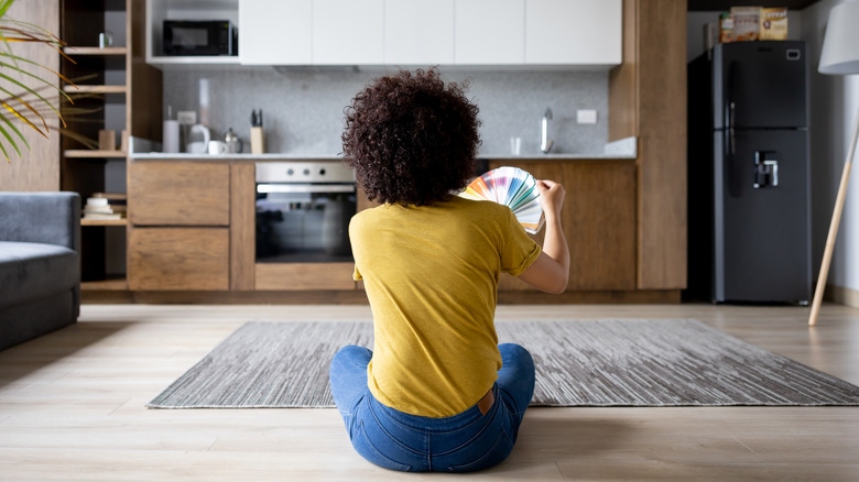 A woman sits on a kitchen floor while looking at bright paint swatches