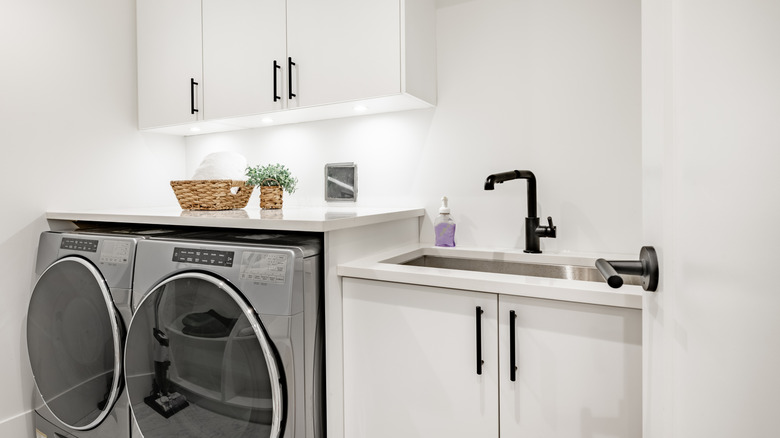 A washer and dryer under cabinets near utility sink with white walls