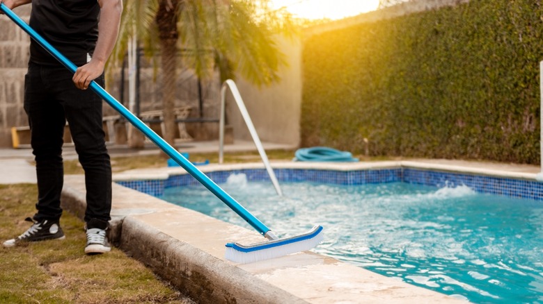 Man brushing sides of pool