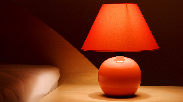 A red-orange lamp with lampshade sitting on end table in bedroom