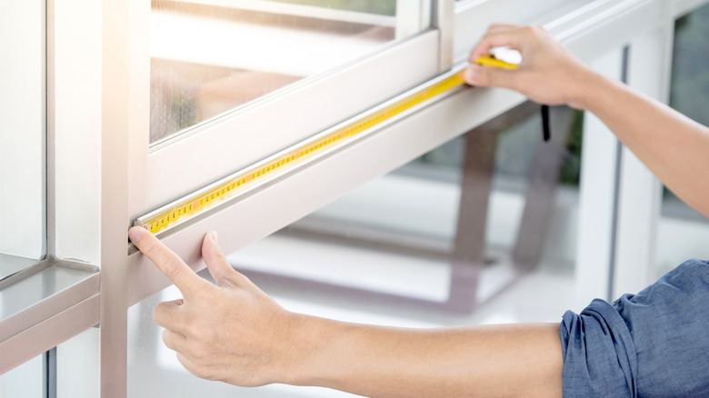 A person measures a window sill using a measuring tape