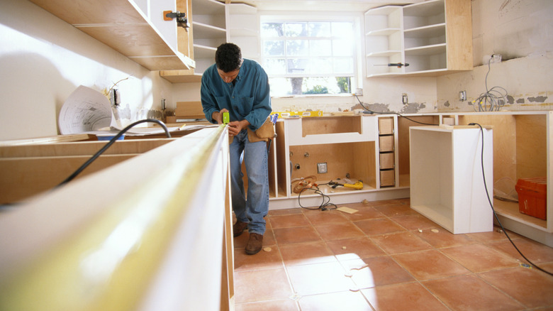 A man stands in a kitchen under construction measuring a countertop