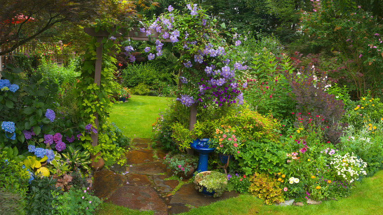 Garden with blooming flowers, archway trellis, and birdbath.