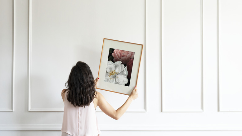 Woman deciding where to hang floral artwork on white wall