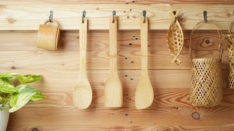 Bamboo kitchen utensils hanging on hooks that are attached to a light wood backsplash