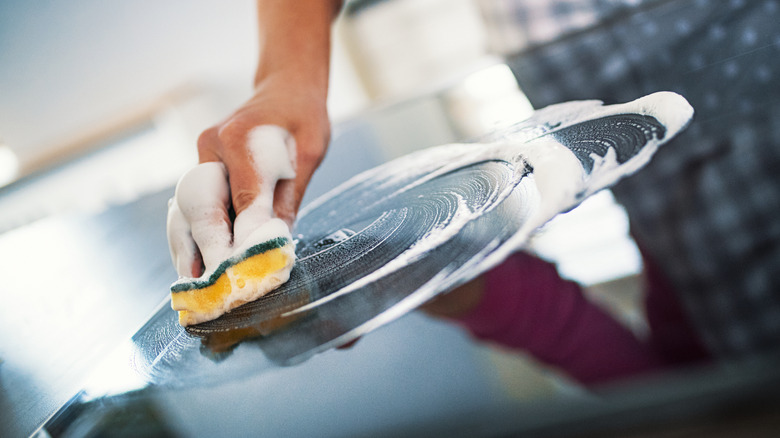 Person washing stove top with sponge