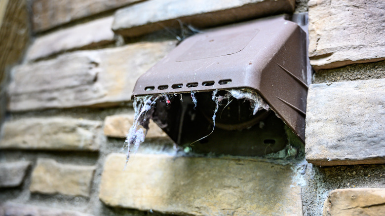 A dirty dryer vent on the exterior of a stone home