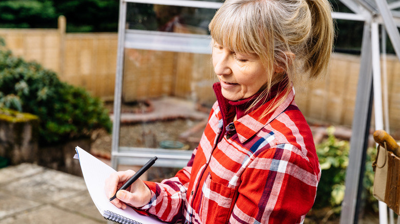 Woman in the garden sketching her plans in a notebook