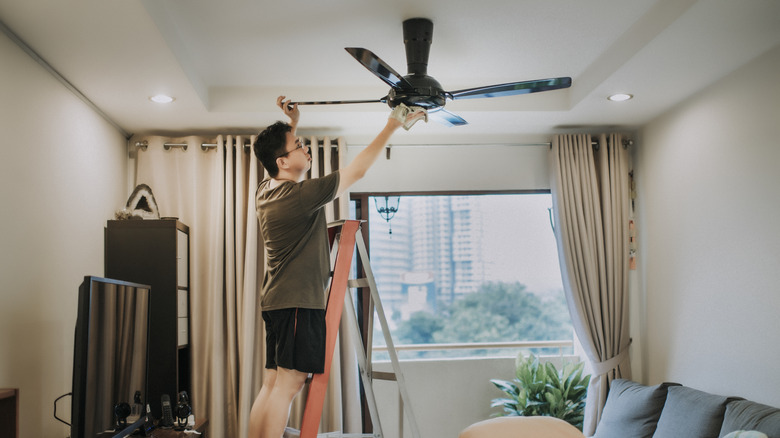 Man standing on a ladder to clean a ceiling fan