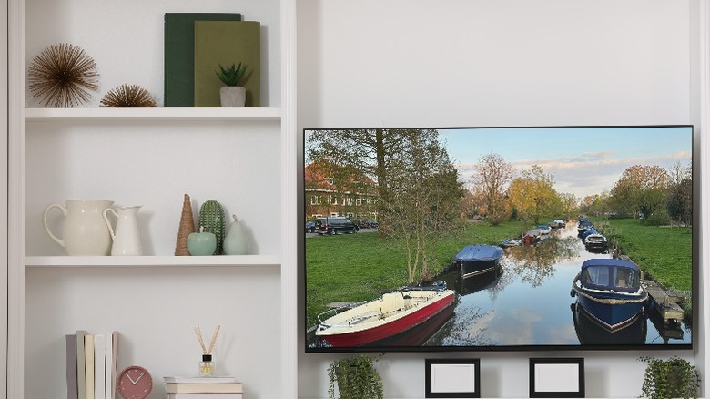 A TV is mounted on a large shelving unit with decorative items around it.