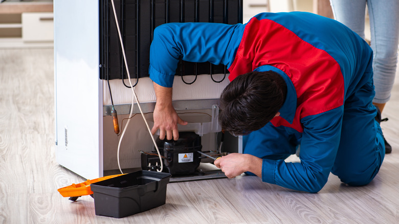 Man cleaning bottom of fridge 