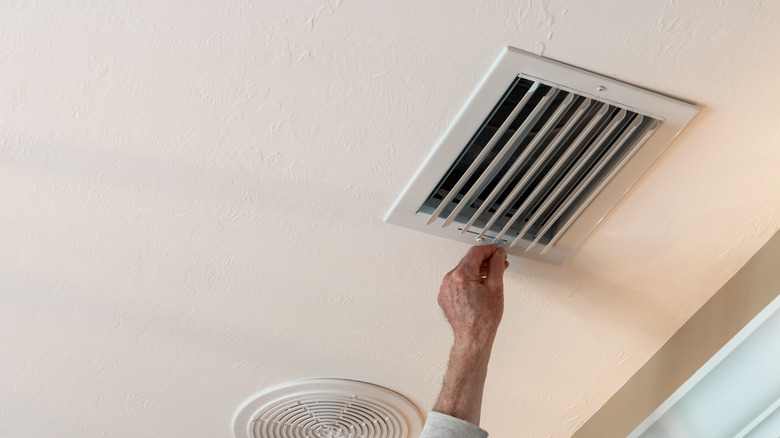 Hand touching air vent on ceiling