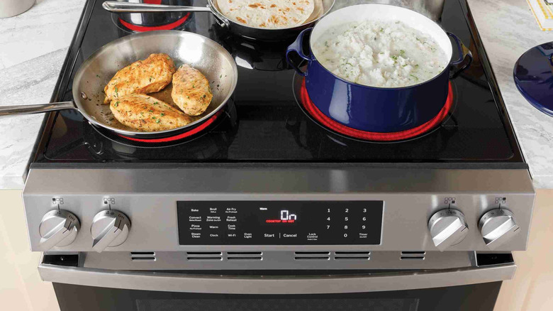 GE range with a stainless steel frying pan containing chicken breasts and blue enamel pot containing rice