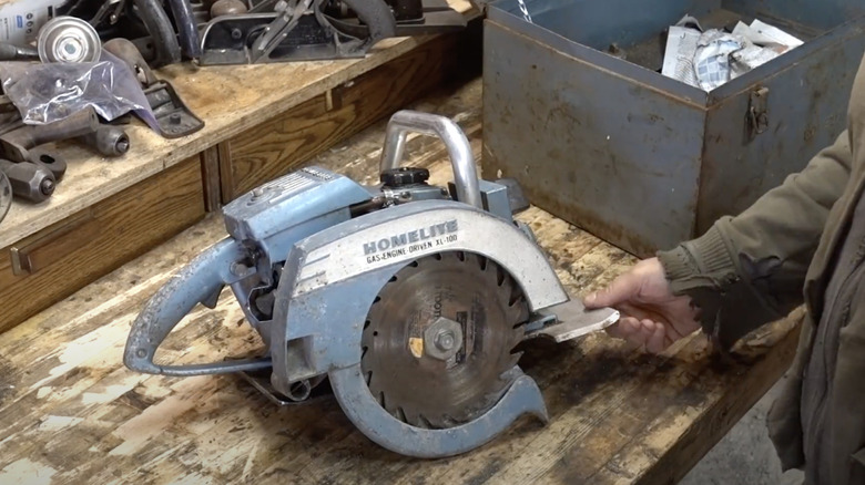 gas-powered saw on wood workbench with man's hand