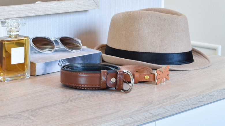 Two belts sitting on a dresser with other accessories