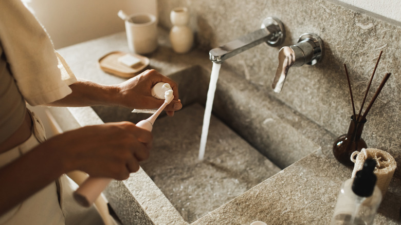 Man with toothbrush in a modern bathroom with a stone sink and countertop.