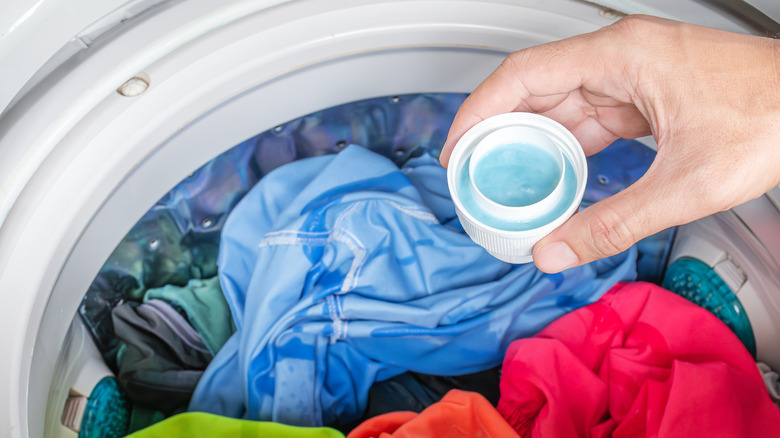 A cap of laundry detergent is held above a full washing machine