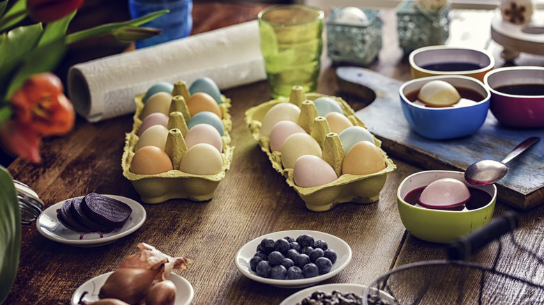 Dozens of pastel eggs sit in cartons on a table surrounded by natural dye baths