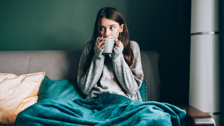 Woman drinking from a mug while sitting under a blanket