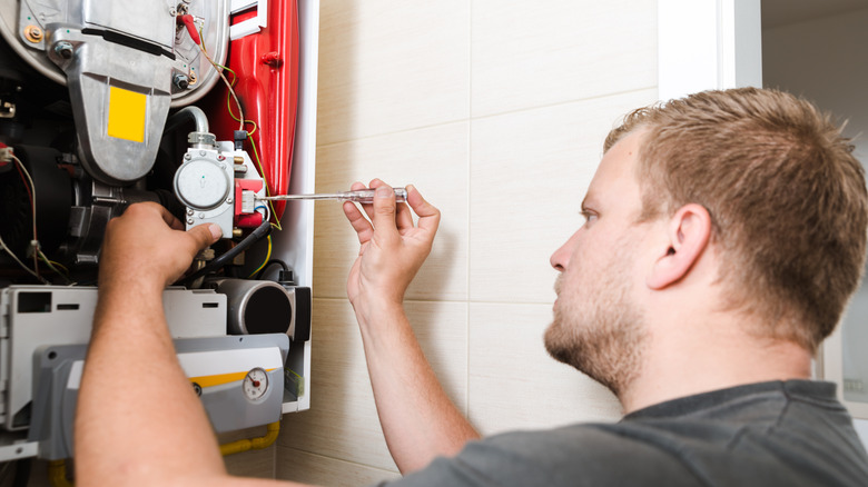 A worker repairing a furnace with a screwdriver