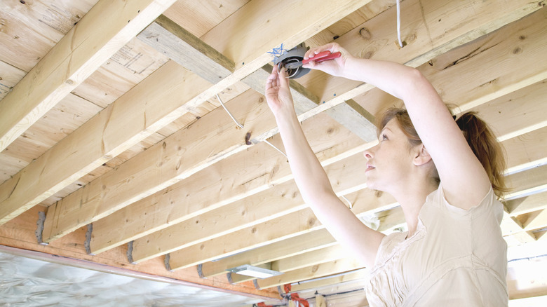 A woman attaching wooden beams to a ceiling.